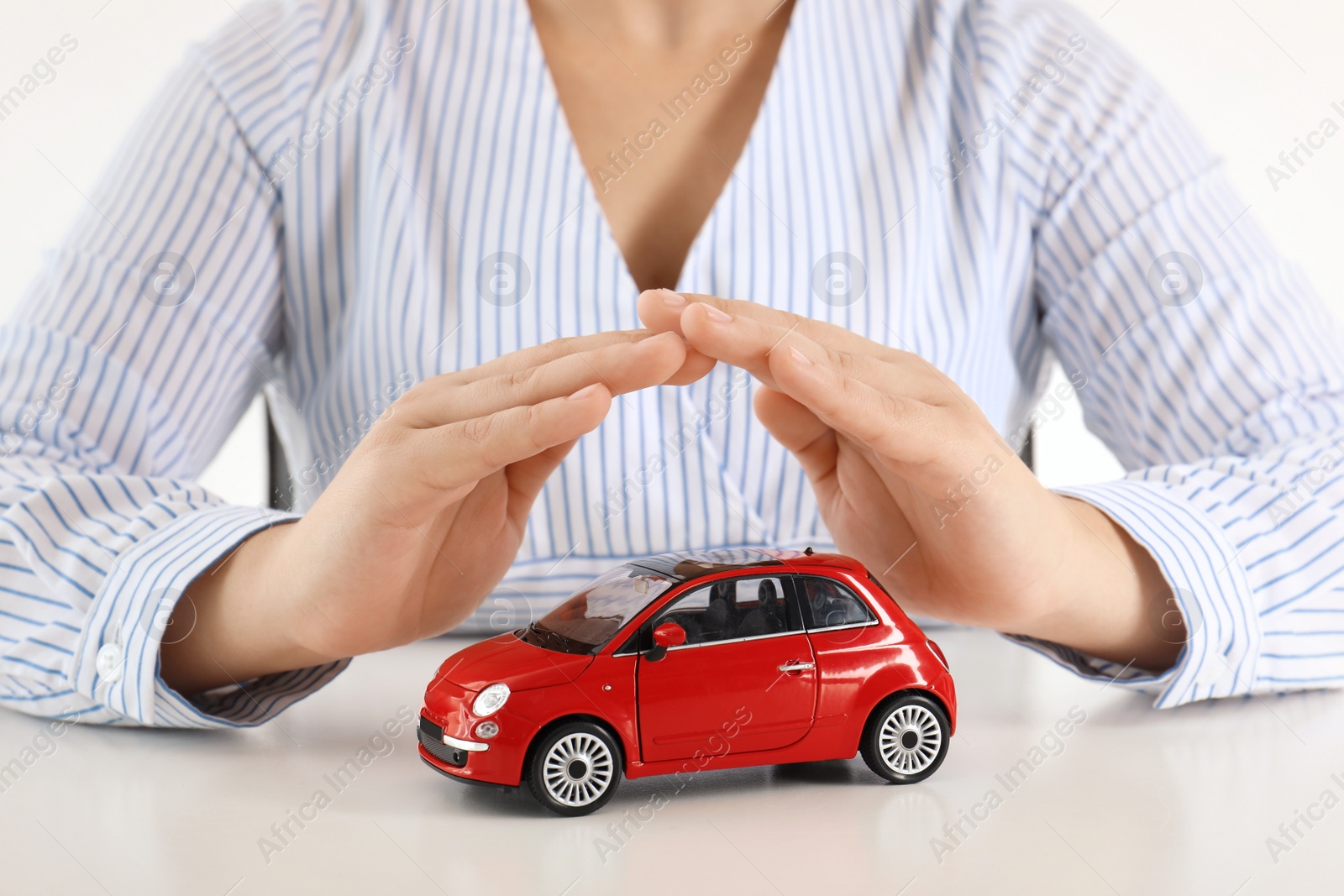 Photo of Female insurance agent covering toy car at table, closeup