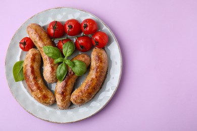 Photo of Plate with tasty homemade sausages, basil leaves and tomatoes on violet table, top view. Space for text