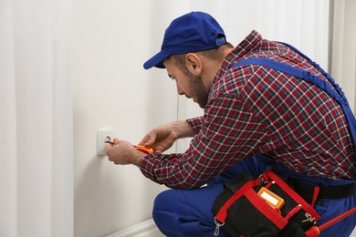 Photo of Electrician with screwdriver repairing power socket indoors