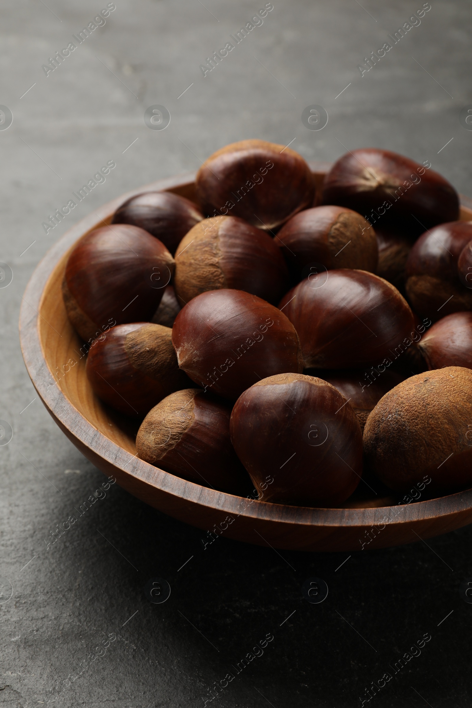 Photo of Roasted edible sweet chestnuts in bowl on grey table, closeup