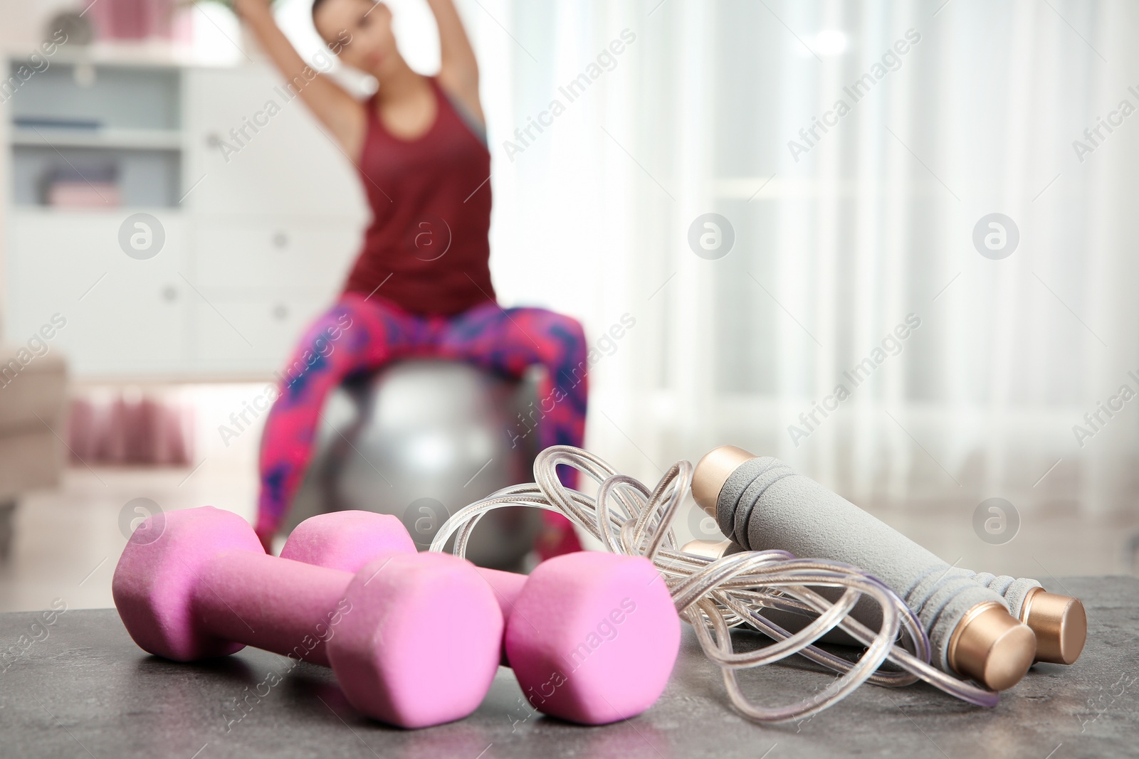 Photo of Woman doing fitness exercise at home, focus on dumbbells and jump rope. Space for text