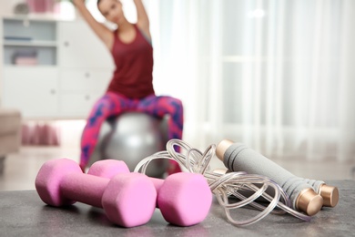 Woman doing fitness exercise at home, focus on dumbbells and jump rope. Space for text