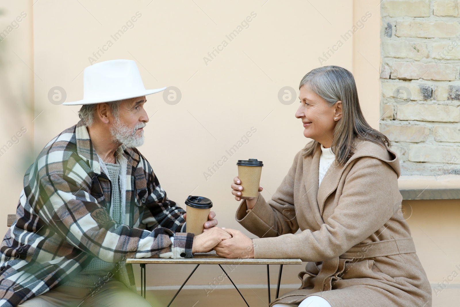 Photo of Affectionate senior couple sitting in outdoor cafe and drinking coffee