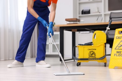 Cleaning service worker washing floor with mop, closeup. Bucket with wet floor sign in office
