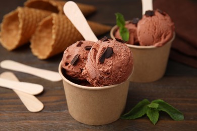 Photo of Paper cups with tasty chocolate ice cream on wooden table, closeup