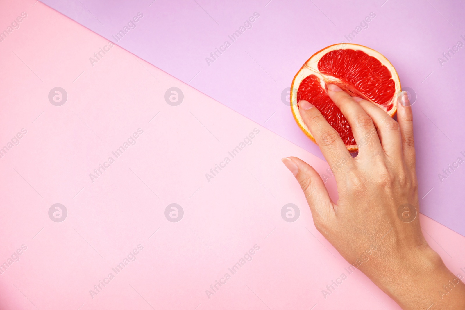 Photo of Young woman touching half of grapefruit on color background, top view with space for text. Sex concept