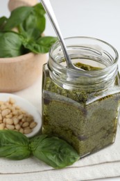 Photo of Tasty pesto sauce in glass jar, spoon, pine nuts and basil on table