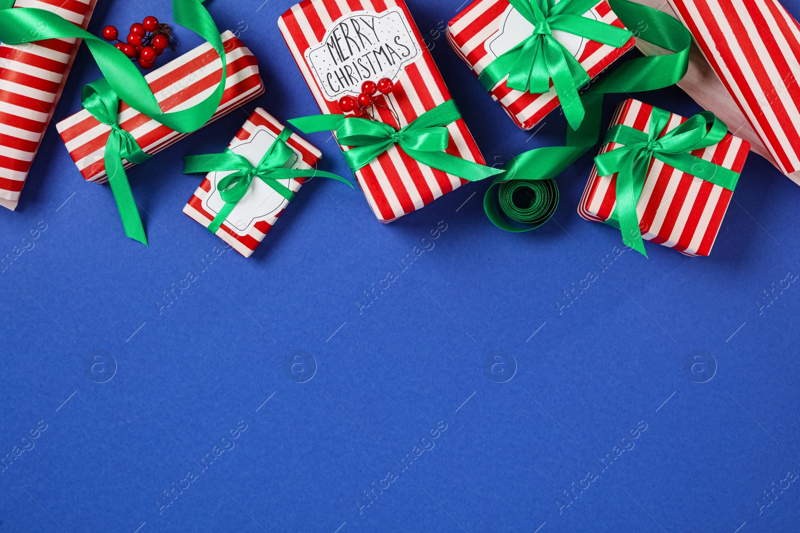 Photo of Christmas gift boxes with green bows on blue background, flat lay. Space for text