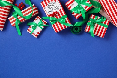 Photo of Christmas gift boxes with green bows on blue background, flat lay. Space for text