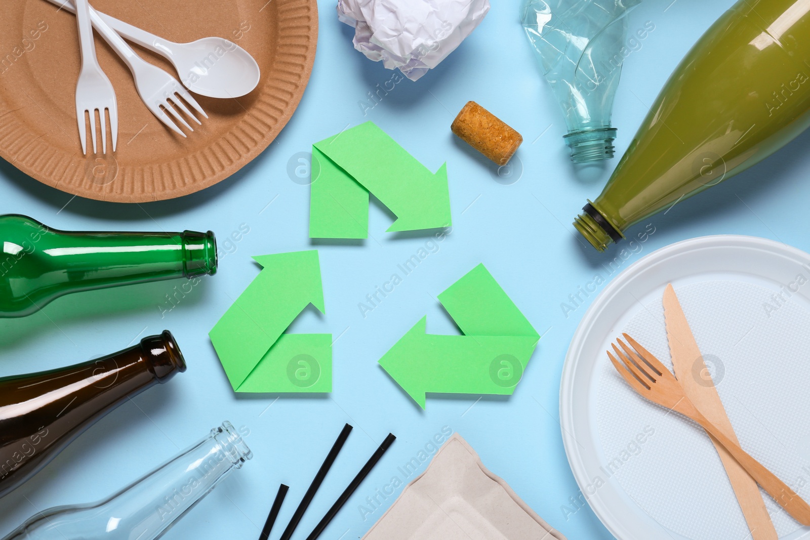 Photo of Recycling symbol, glass and plastic items on light blue background, flat lay