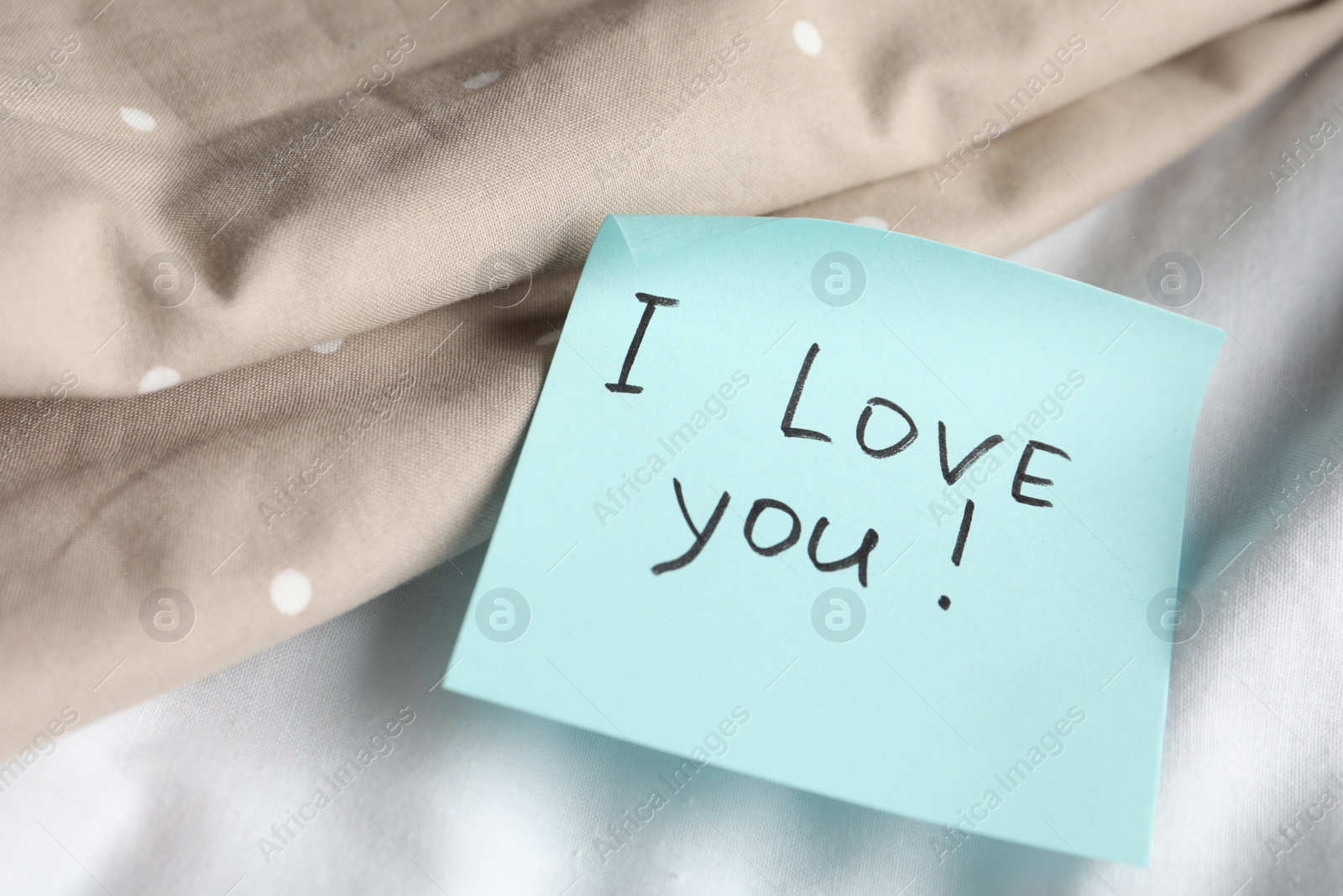 Photo of Sticky note with phrase I love you! on bed, closeup