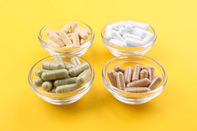 Photo of Different vitamin capsules in glass bowls on yellow background