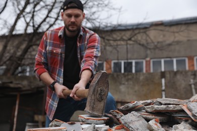 Photo of Man breaking bricks with sledgehammer outdoors, selective focus. Space for text