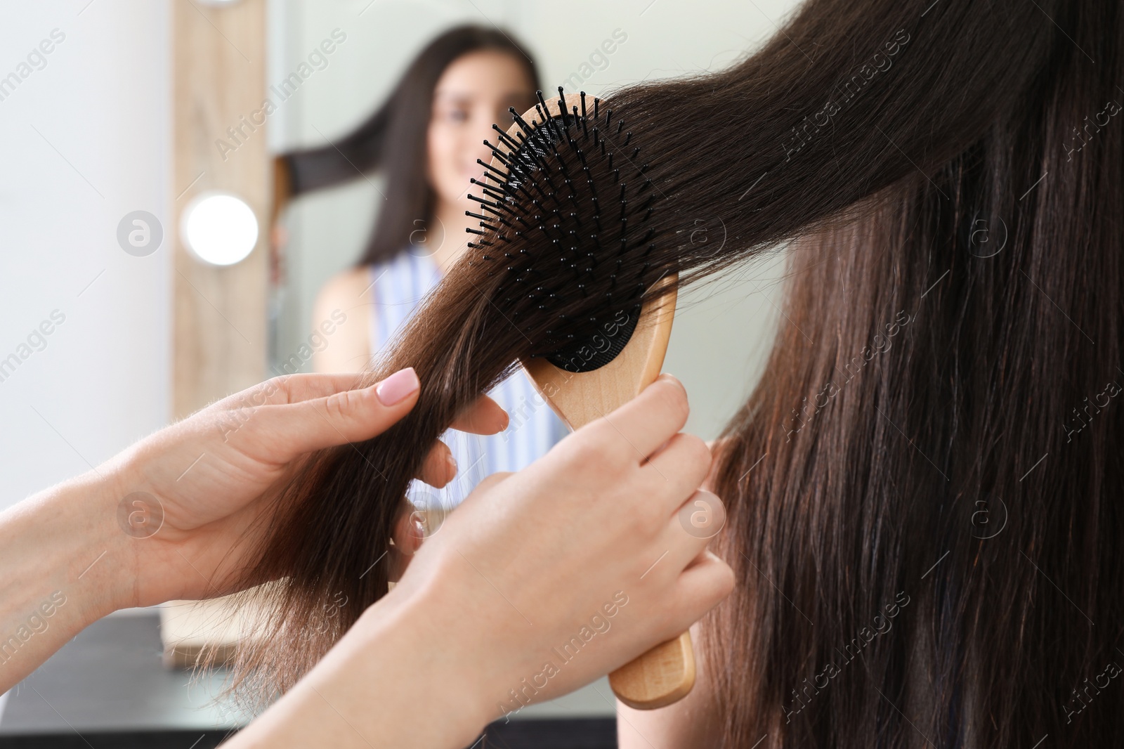 Photo of Woman combing friend's hair with cushion brush indoors, closeup