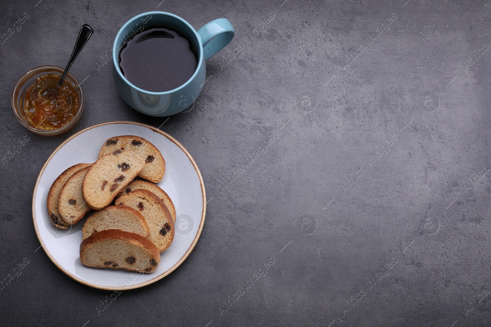 Photo of Sweet hard chuck crackers with raisins, jam and cup of tea on grey table, flat lay. Space for text