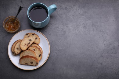 Photo of Sweet hard chuck crackers with raisins, jam and cup of tea on grey table, flat lay. Space for text