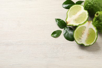 Whole and cut ripe bergamot fruits with green leaves on white wooden table, flat lay. Space for text