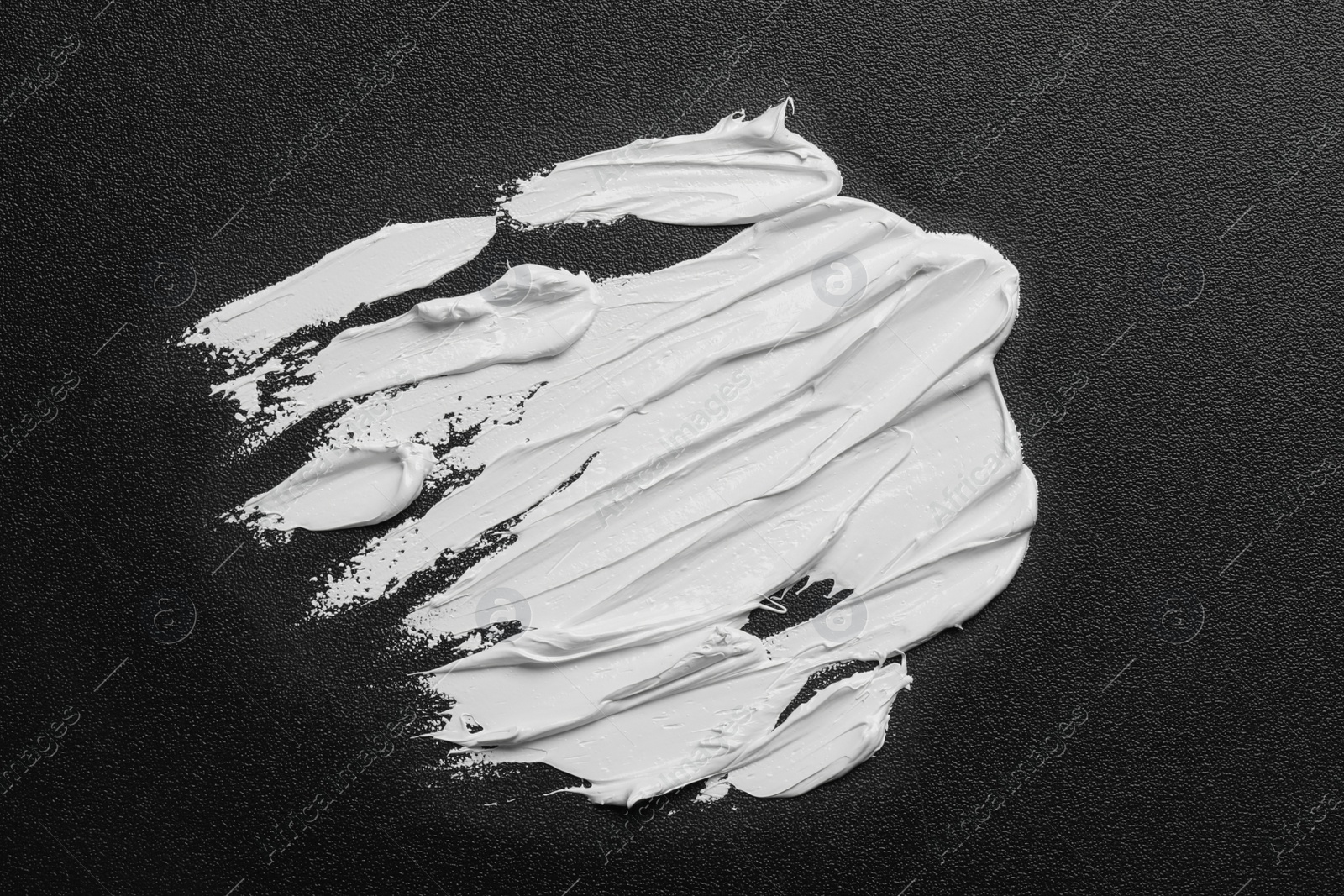 Photo of Strokes of white oil paint on black canvas, top view