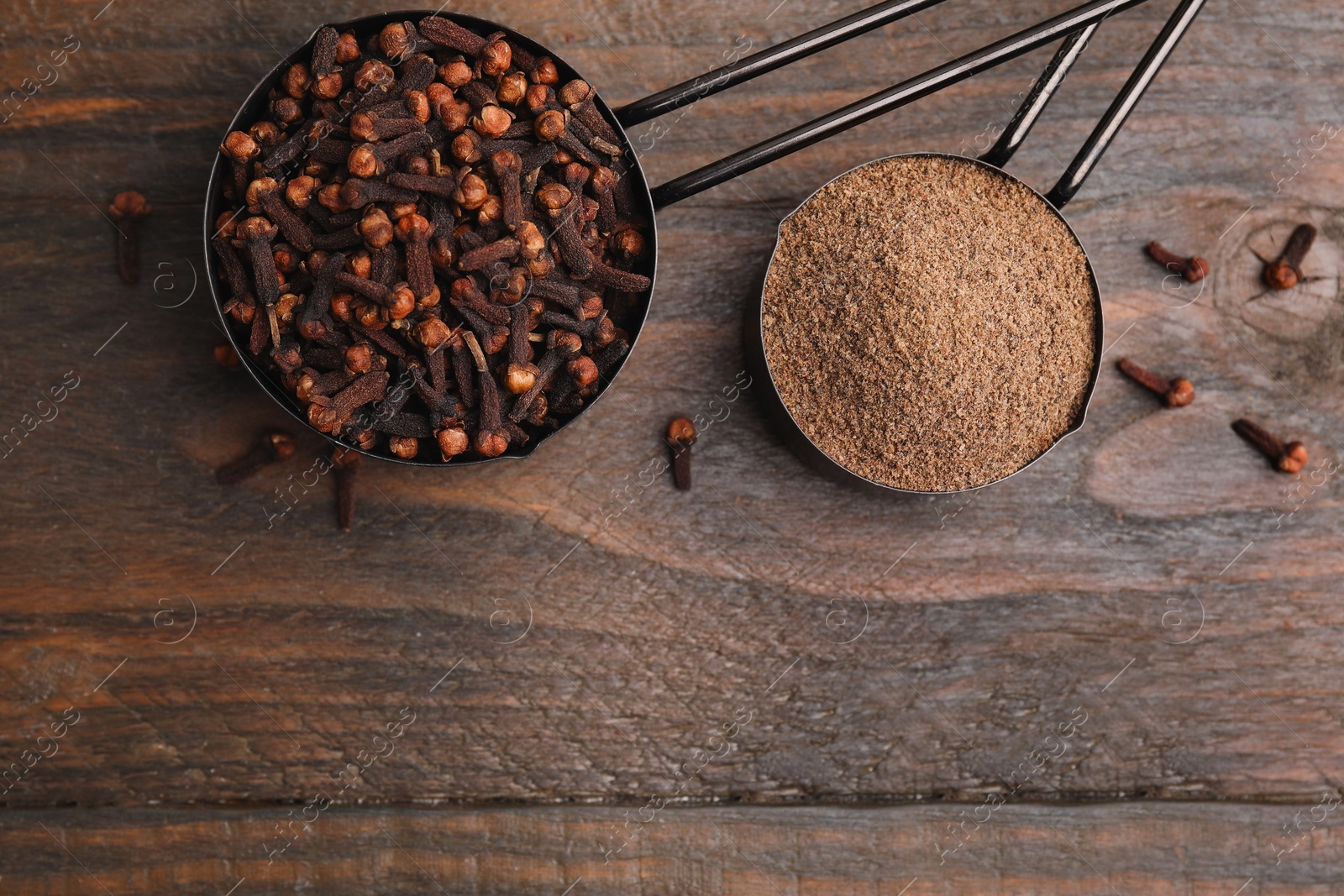 Photo of Aromatic clove powder and dried buds in scoops on wooden table, top view. Space for text