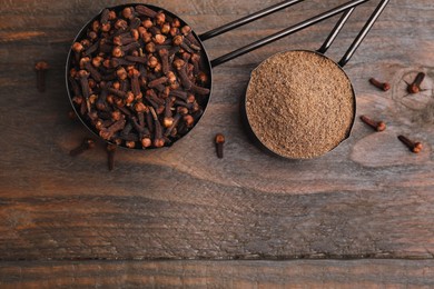 Photo of Aromatic clove powder and dried buds in scoops on wooden table, top view. Space for text