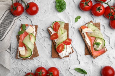 Photo of Tasty rye crispbreads with salmon, cream cheese and vegetables on grey textured table, flat lay