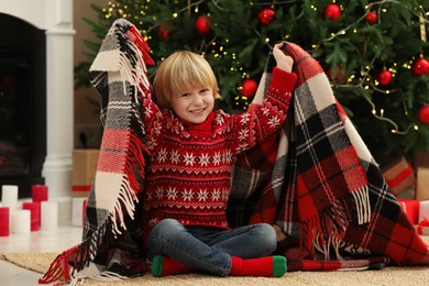 Photo of Little child with plaid on floor near Christmas tree at home