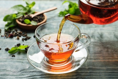 Pouring black tea into glass cup on wooden table