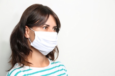 Young woman in protective face mask on light background, space for text