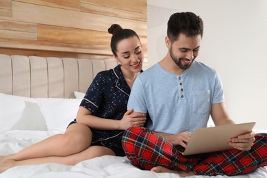 Photo of Happy couple in pajamas with laptop on bed at home