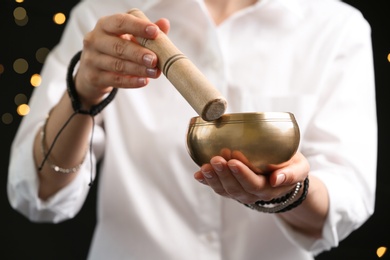 Photo of Woman using singing bowl in sound healing therapy on black background, closeup