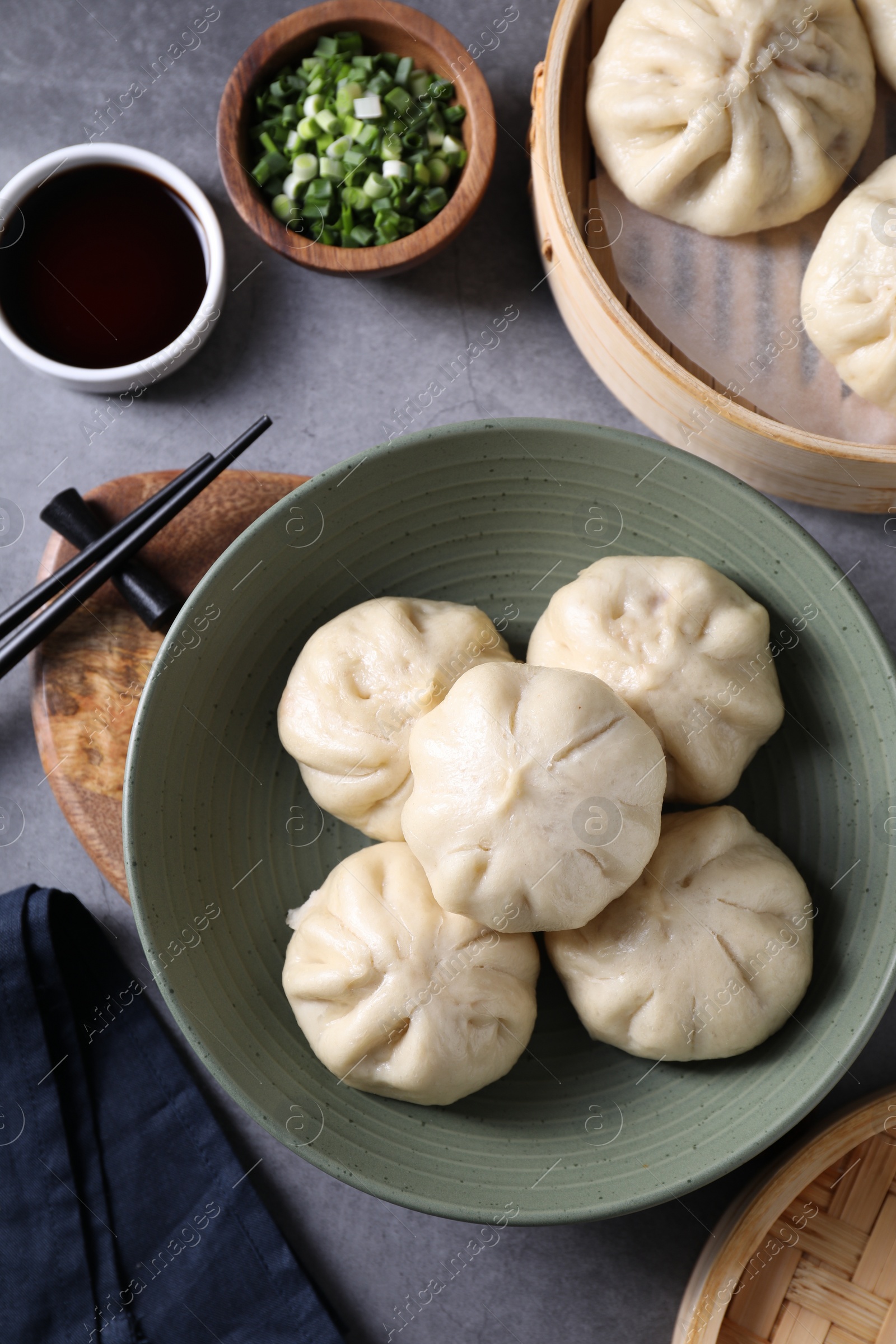 Photo of Delicious bao buns (baozi), chopsticks, soy sauce and green onion on grey table, flat lay