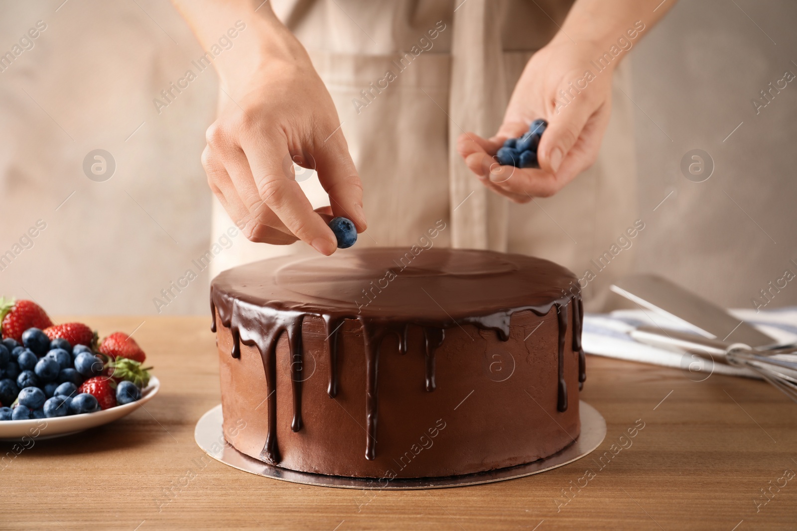 Photo of Baker decorating fresh delicious homemade chocolate cake with berries on table, closeup