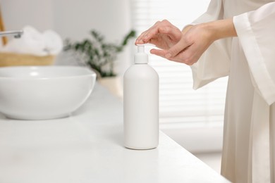 Young woman using body cream in bathroom, closeup