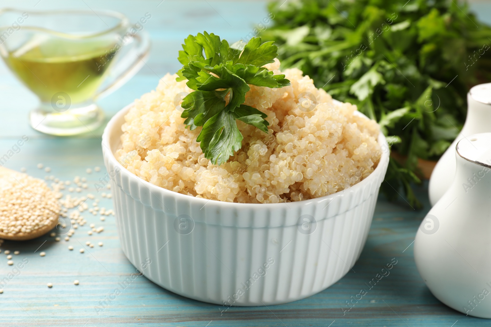 Photo of Tasty quinoa porridge with parsley in bowl on light blue wooden table, closeup