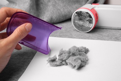 Woman holding fluff collector of fabric shaver and lint on light grey cloth, closeup