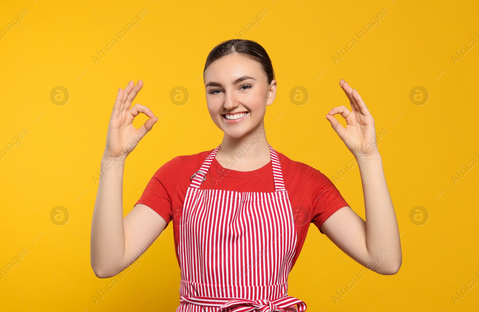 Photo of Beautiful young woman in clean striped apron on orange background