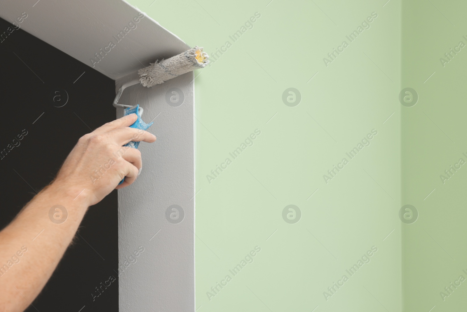 Photo of Worker using roller to paint wall with white dye indoors, closeup