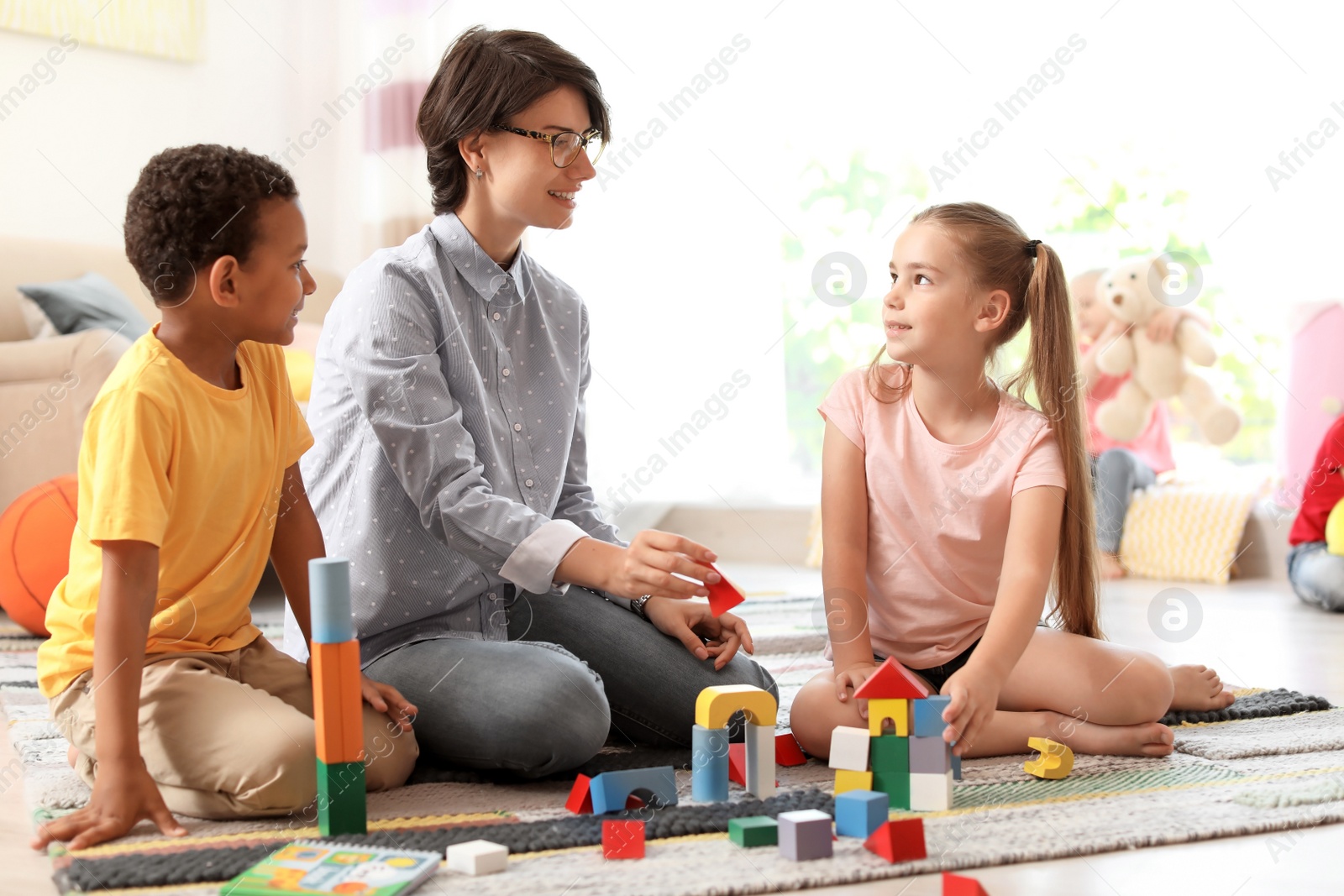 Photo of Young woman playing with little children indoors
