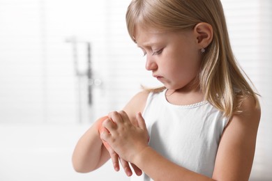 Photo of Suffering from allergy. Little girl scratching her hand indoors, space for text