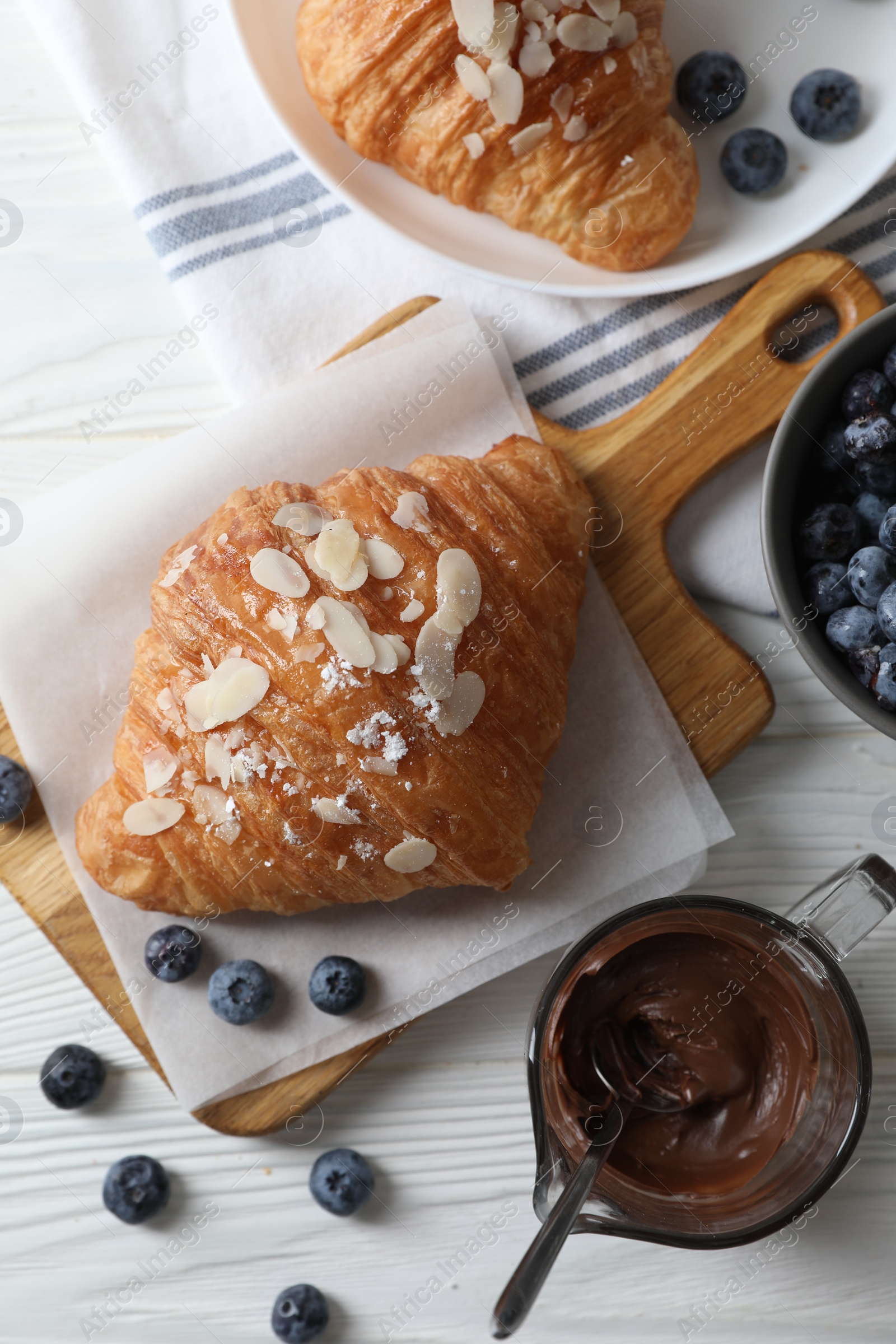 Photo of Delicious croissants with almond flakes, chocolate and blueberries served on white wooden table, flat lay