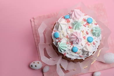 Traditional Easter cake with meringues and painted eggs on pink background, above view. Space for text