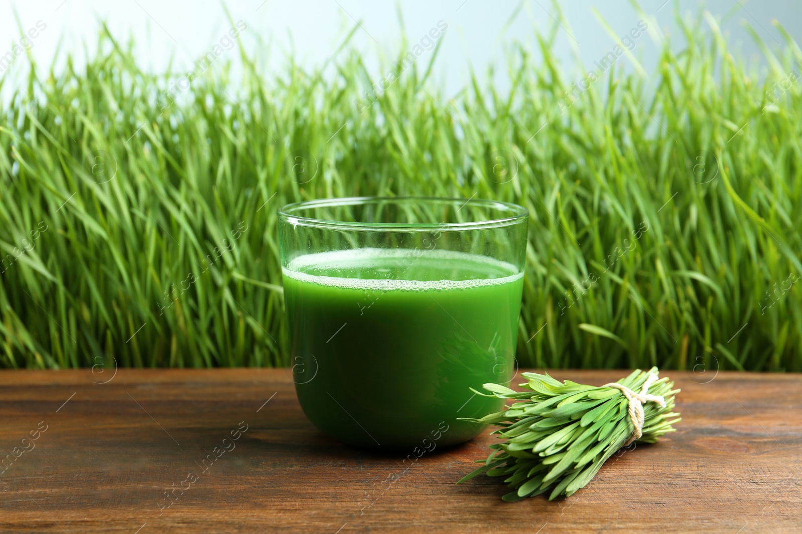 Glass of juice on wooden table near fresh wheat grass Photo of Glass of juice on wooden table near fresh wheat grass
