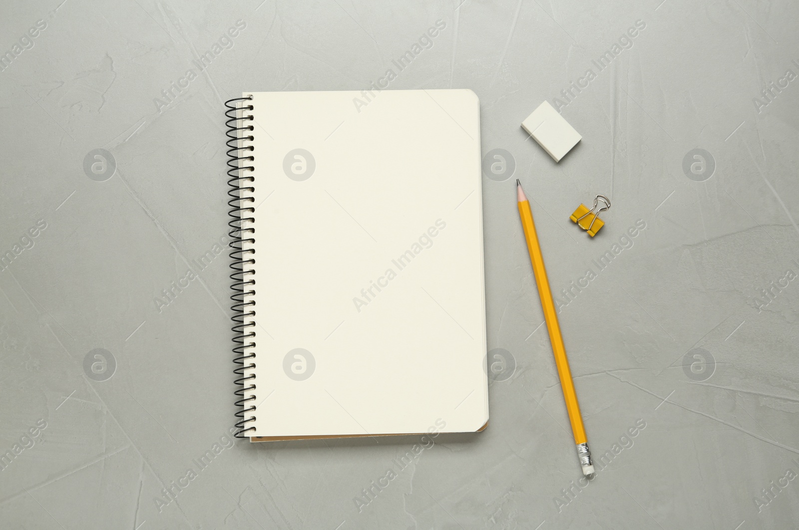 Photo of Sketchbook, pencil, clip and eraser on light grey table, flat lay