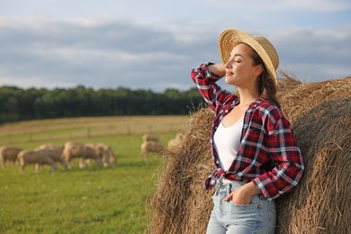 Photo of Beautiful woman near hay bale on farm. Space for text