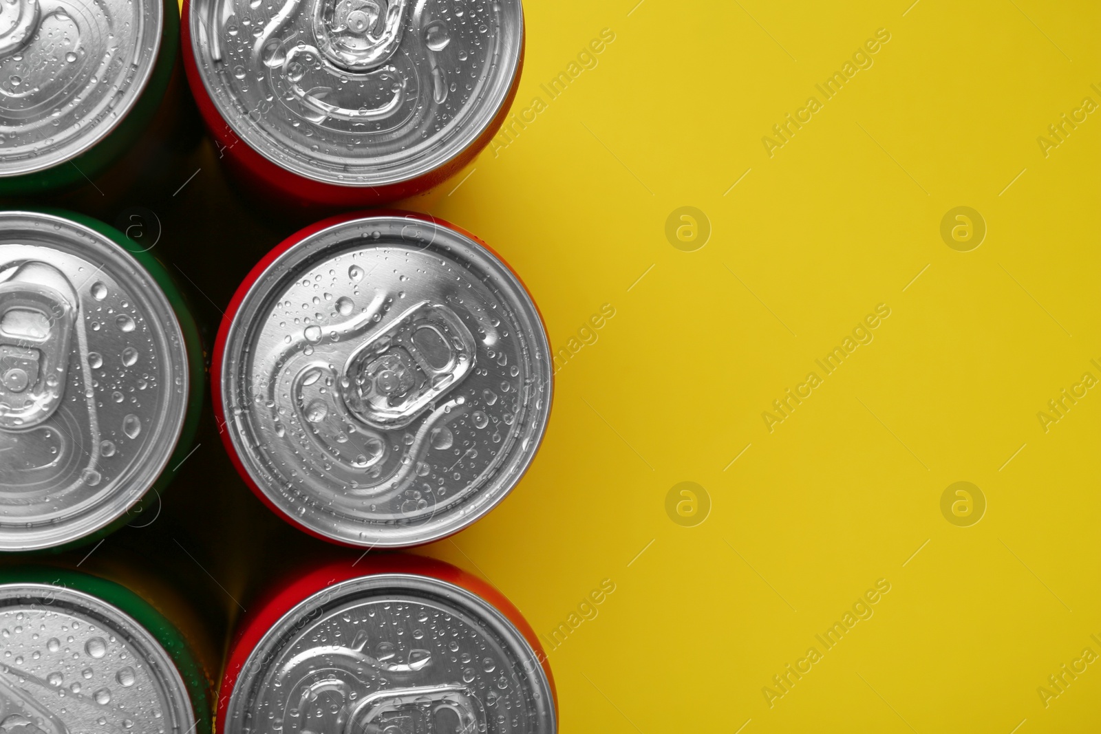 Photo of Energy drinks in wet cans on yellow background, top view. Space for text