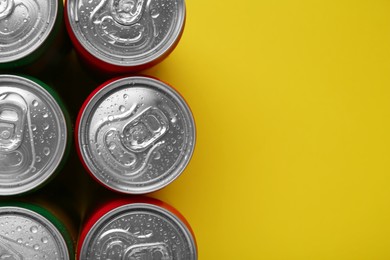 Energy drinks in wet cans on yellow background, top view. Space for text