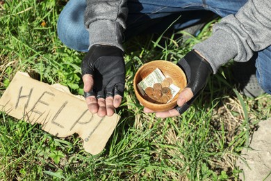 Photo of Poor homeless man holding bowl with donations near help sign outdoors, closeup