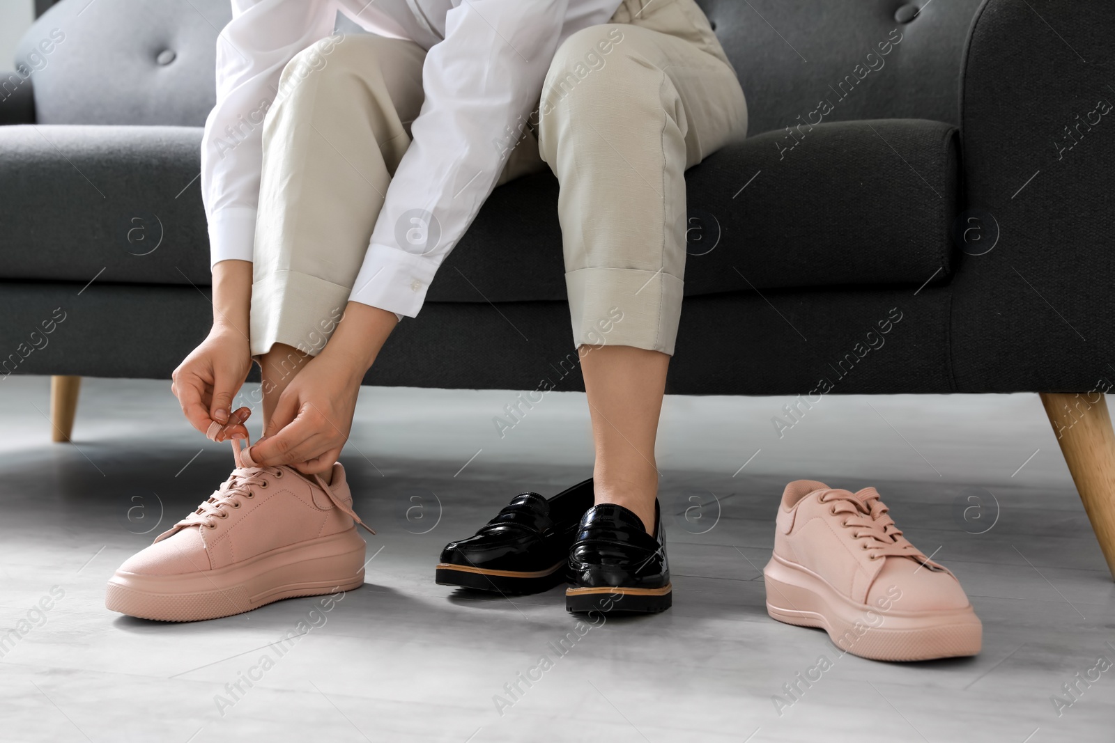 Photo of Woman taking off uncomfortable shoes and putting on sneakers in office, closeup