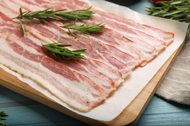 Photo of Slices of raw bacon and rosemary on light blue wooden table