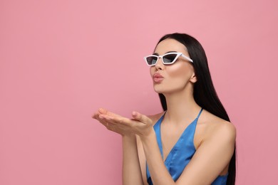 Photo of Beautiful young woman in stylish sunglasses blowing kiss on pink background. Space for text
